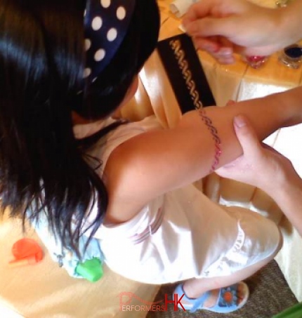 A tattoo artist is getting the a arm glittering tattoo done for a girl at a school fair. 