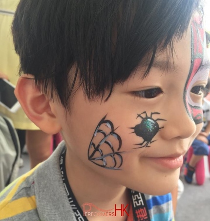 HK face painter draw a spider face paint on a kid face at a corporate Halloween event