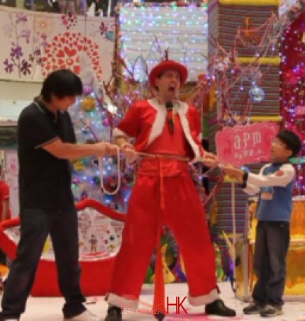 A Hong Kong funny clown performing the rope through the body trick with two volunteer helper from the audience , the try to pull the rope with tight on the entertainers body at a Xmas shopping mall function