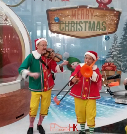 Xmas band trio playing with santa sitting in giant snow globe in background.