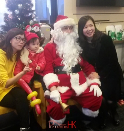 Santa with two ladies and a baby sitting in front of a Christmas tree at a Kong Kong corporate event.