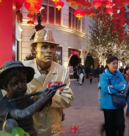 Golden statue standing next to bronze statue of boy playing the flute