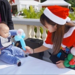genie in red santa girl costume twisting balloons for baby